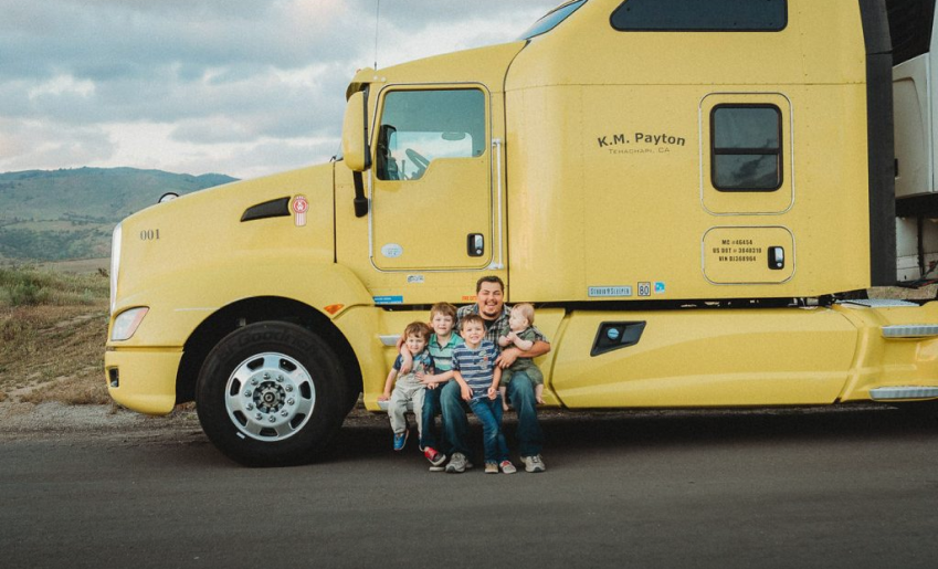 Owner Operator Mike Payton holds his four young children in front of his semi truck