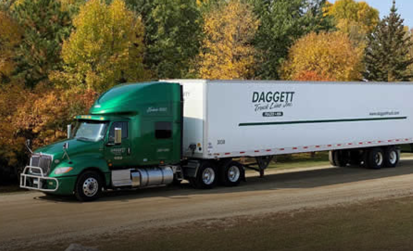 Green cab and Daggett branded trailer are parked in front of fall colored trees